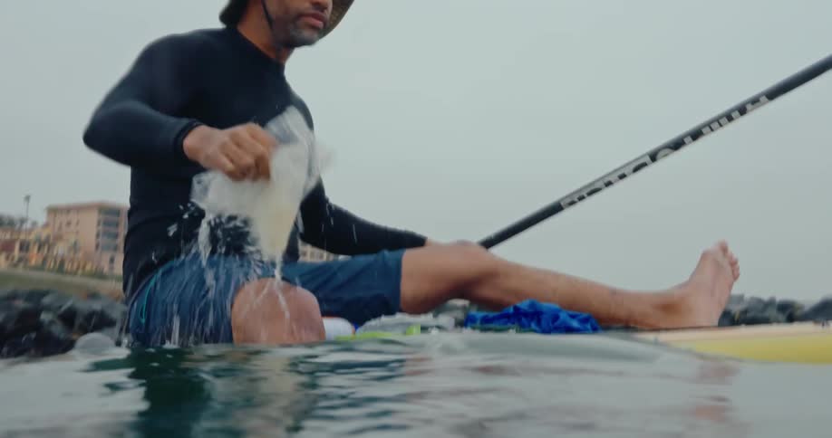 A man is floating on a surfboard and removing trash from the ocean
