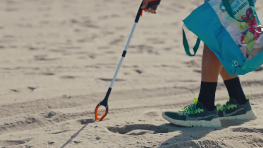 Person with a tool for picking up trash in the sand on the beach