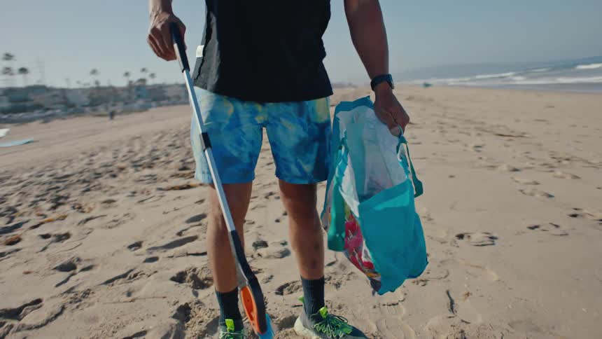 Two men using pickers to pick up trash from a beach sand and put it in a plastic bag