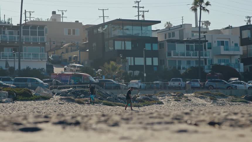 Two people picking up garbage from a beach next to the city