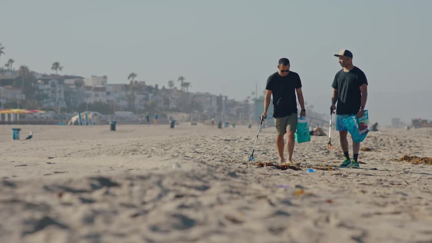Two men are cleaning up a beach by picking up pieces of trash