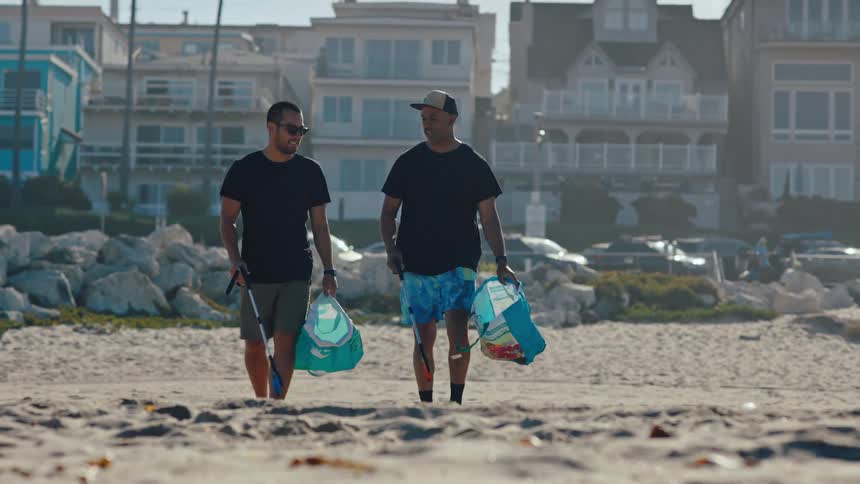 Two men with garbage bags collecting trash from the sand on the beach