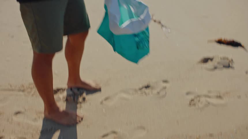 Two men walk on the beach picking up trash talking and smiling