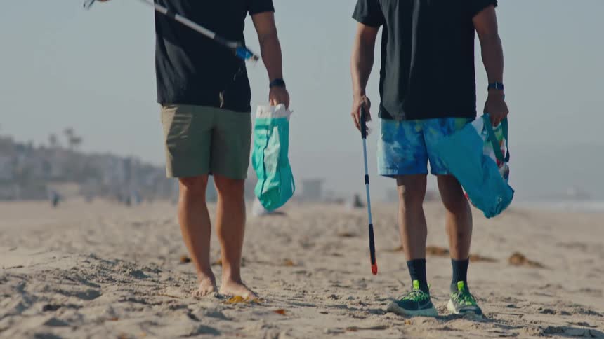 Two men walking on the sand at the beach collecting trash