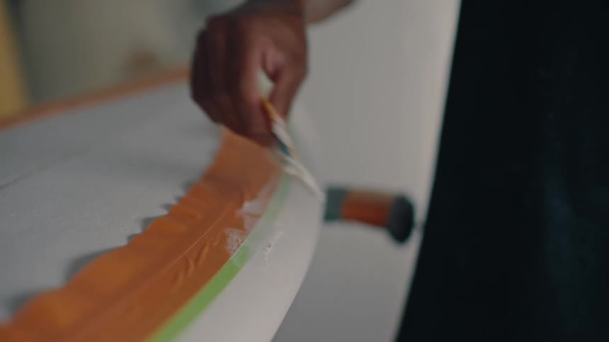 Man hand with a spatula finishing off the side of a surfboard with paint