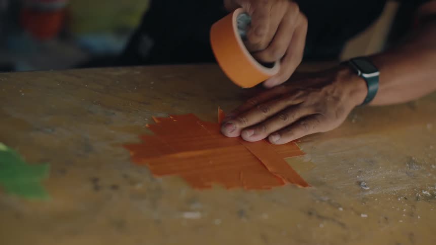 A person putting orange tape to fix the surface of a surfboard