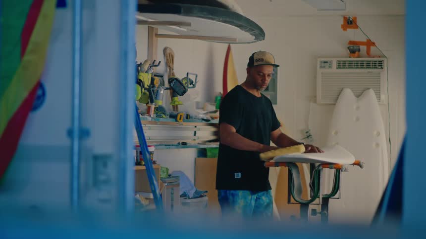 An individual waxes a surfboard which is placed on supports
