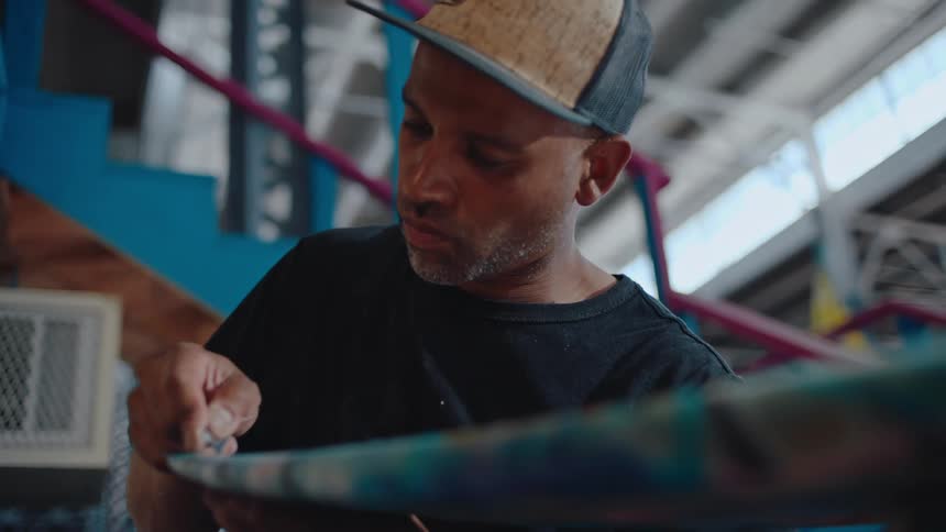 A male employee uses a razor blade to cut the edge of a surfboard
