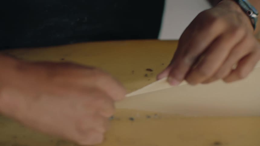 Closeup of hands peeling off the old coating from a surfboard