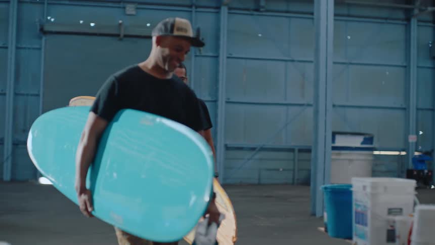 Two men holding surfboards and they are walking one of them puts the board on the ground