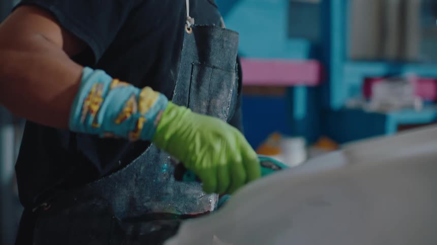 Man in cap and using green disposable gloves working on a surfboard