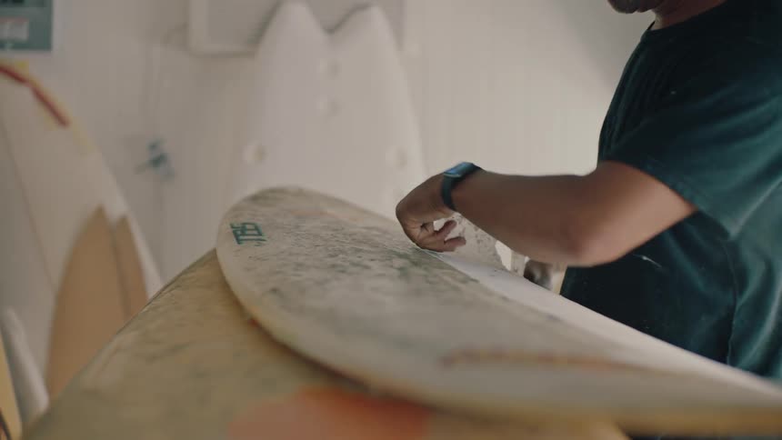 A man peels the finish off a surfboard