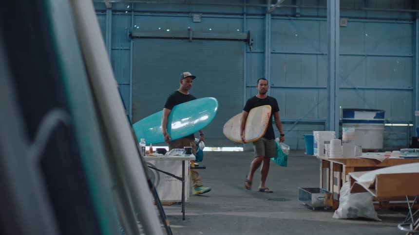 Two men arriving at a place with two surfboards and two bags in their hands and they put this coloring on the floor and one of them puts the board on a table