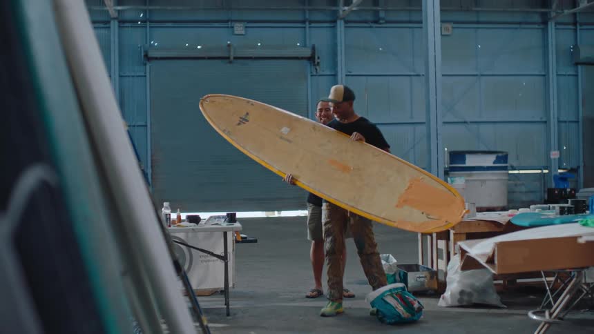 A man hands a surfboard over to a person who works on them