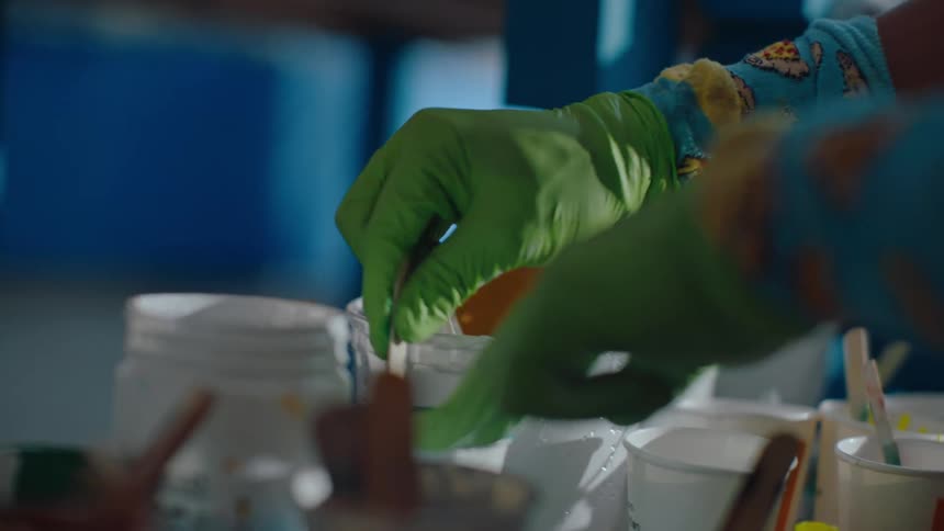 Closeup view of hands wearing green latex gloves mixing paint in small containers with a stick
