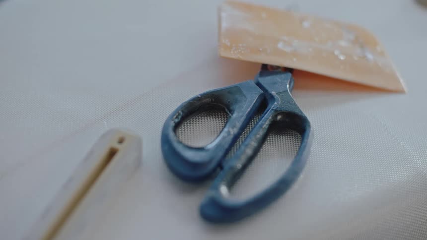 A closeup of scissors and a plastic scrapper over a white textured fabric