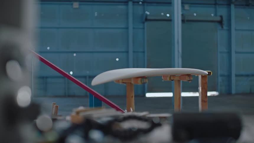 An unfinished surfboard rests over supports inside a workshop