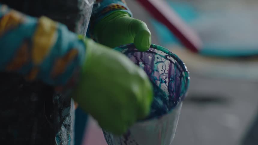 Artist standing in a workshop mixes paint in a small bucket