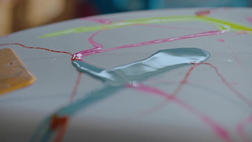 Different colored paints form an abstract pattern on a white surfboard