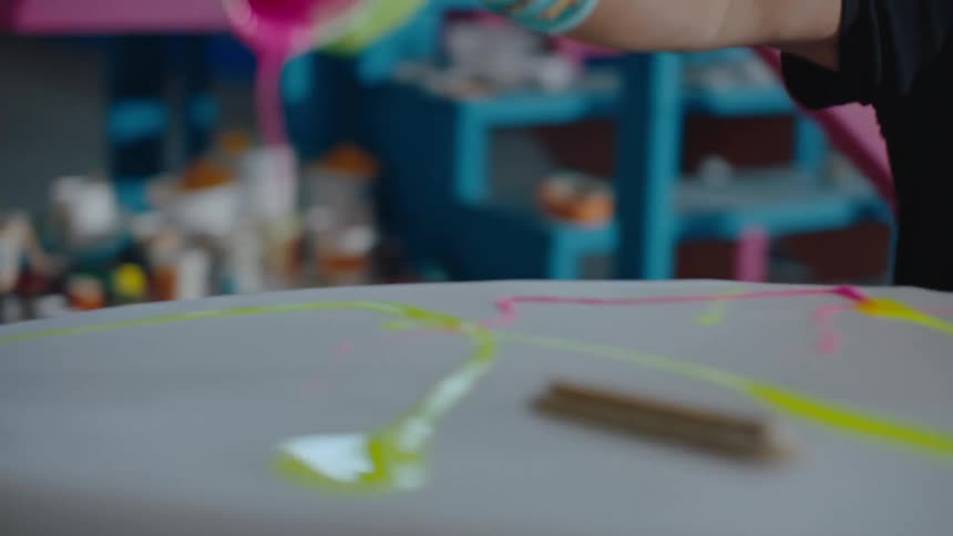 A person with gloves is pouring a cup with a cup of pink paint onto a surface with a white sheet