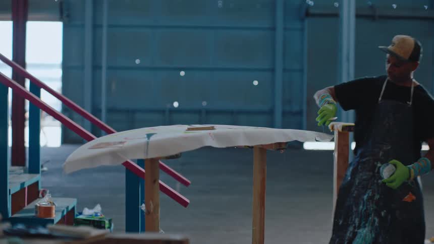 Man in cap putting paint on top of a surfboard