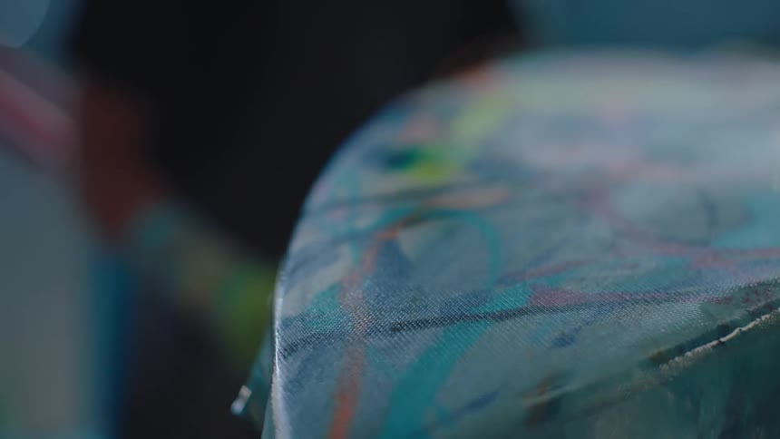 A person with a glove scraping the surface of a colorful surfboard