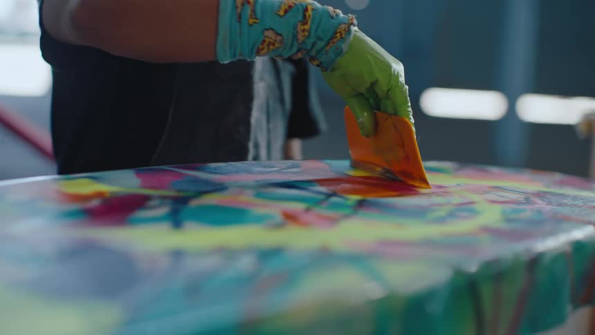 Hand holding a spatula and a bucket pouring a clear liquid onto a surfboard