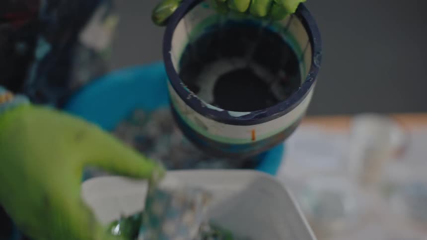 Artist working in a workshop scoops small colored pieces into a small tub