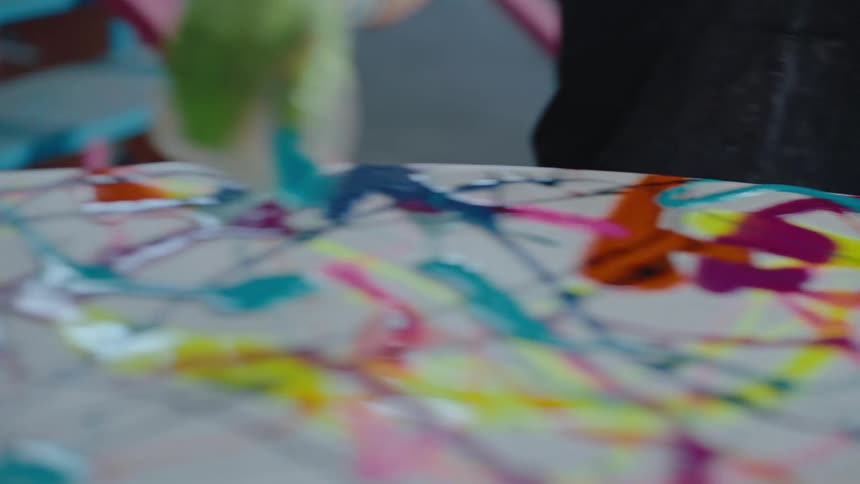 Gloved hand holding a cup that pours paint onto the surface of a surfboard