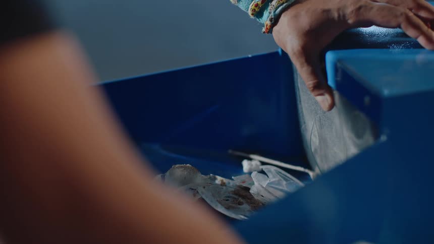Closeup of hands taking out small bits of trash and placing them into a blue container