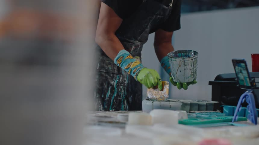 A person engaged in the process of spreading a coat of paint using a plastic scrapper