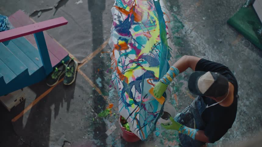 Top view of a man in a cap painting a surfboard