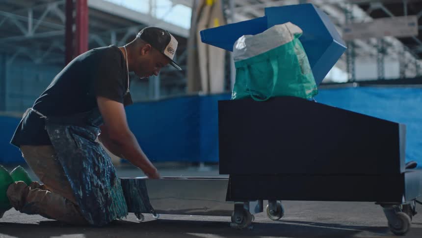 A person in a workshop kneeling beside a container sifting a white substance with his hands
