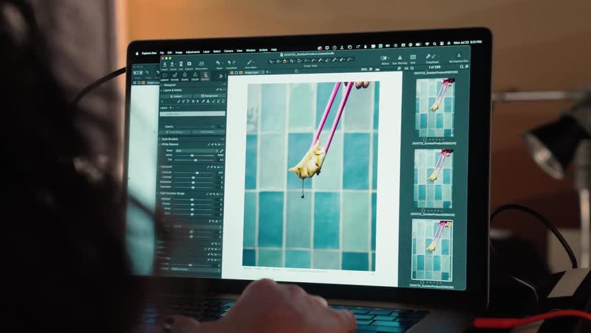A persons hand working on a laptop with the screen on and turned on in image editing software