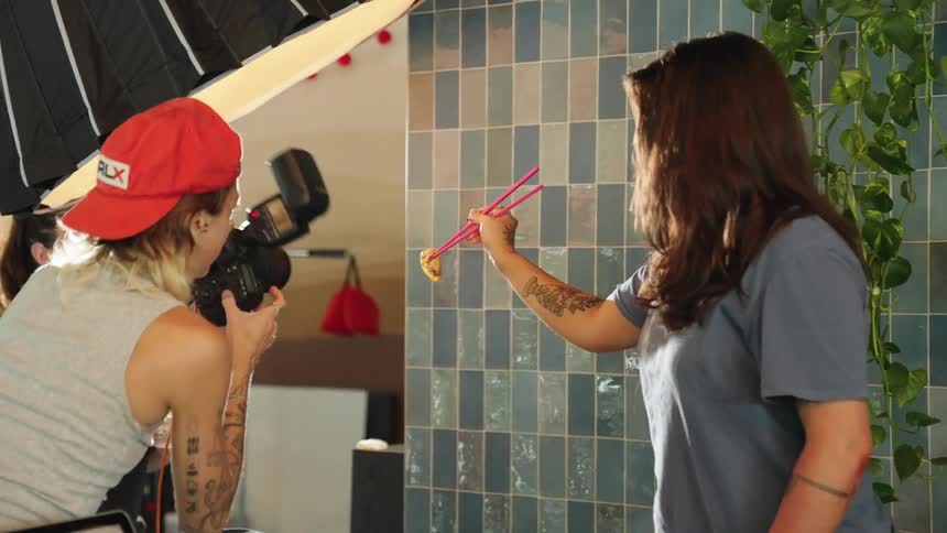 A photographer takes pictures of a dumpling hanging from a chopstick on a restaurant set