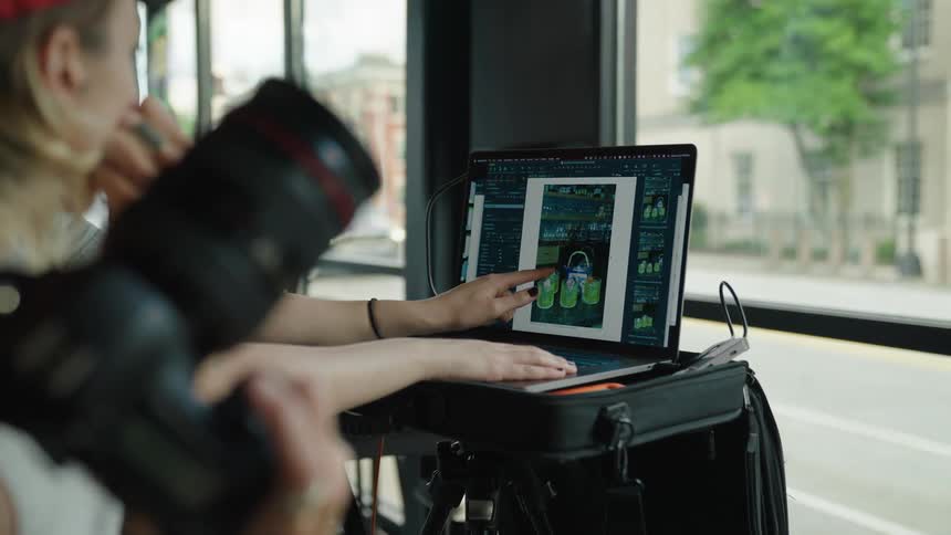 A photographer reviewing pictures on a laptop screen next to a large window overlooking city streets