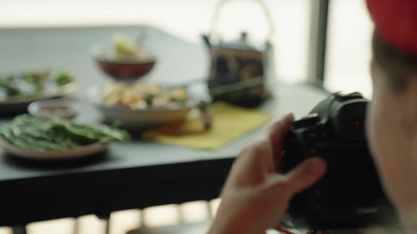 A closeup of a dining table featuring various asian dishes with a photographer capturing pictures