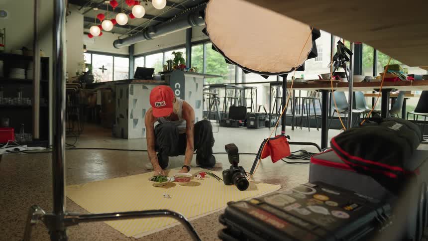 A woman in a red cap is crouched down arranging a small object in a photography studio