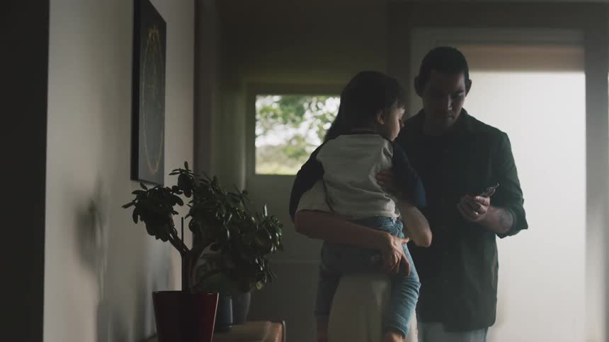 Man showing cell phone to his wife who picks up their son and the three hug