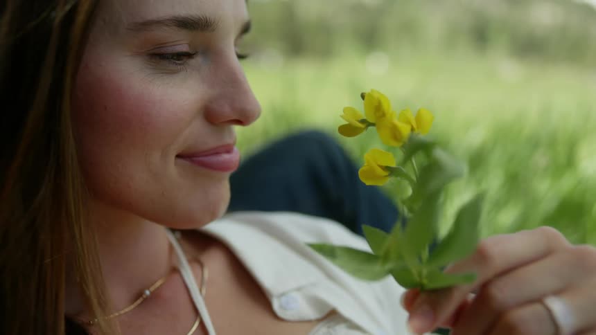Woman sitting in a field placing a yellow flower in her ear