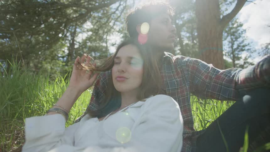 Man and woman lean against each other while sitting on the ground among conifer trees