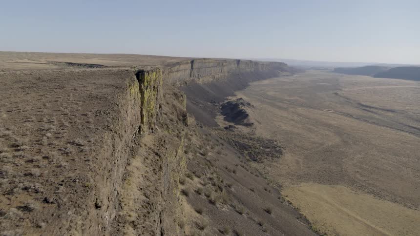 Skimming along the edge of a sheer cliff wall high above a hot and dry desert valley