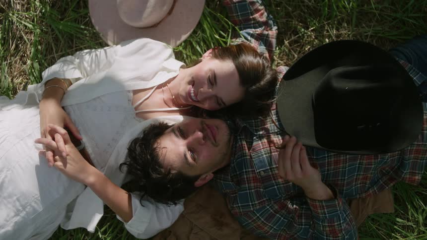Man and woman lying down leaning on each others shoulders while standing on a grass in a field