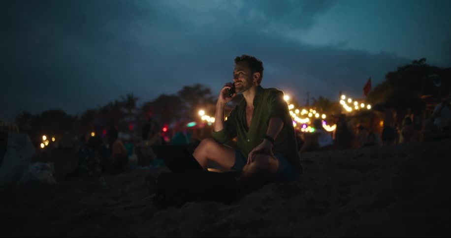 A man talks on his phone while sitting in the sand