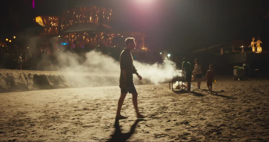 A man walking on a beach at night with several people in the background