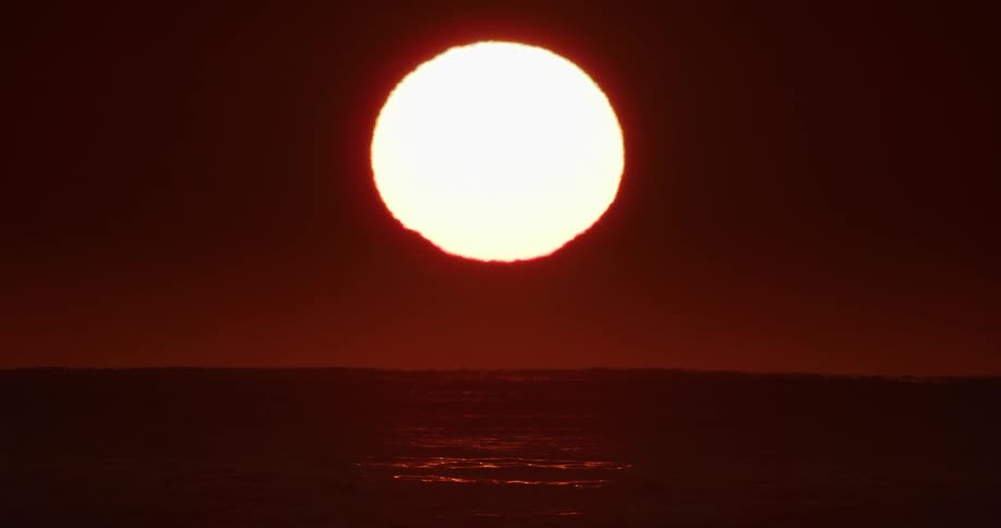 Sun highlighted in a reddish sky rising above sea level