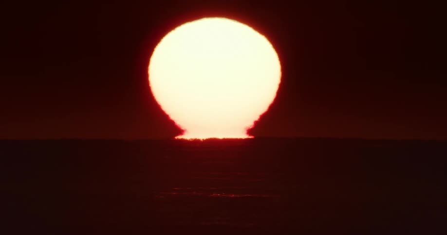 The sun rises on the horizon over the ocean dark red hues across the sky