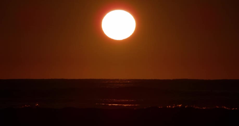 Panorama of a sun rising above sea level against a reddish sky