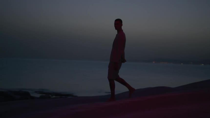 A young man walks along a beach at dusk
