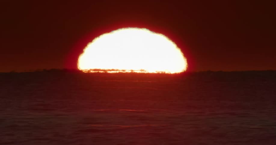 A vibrant sunrise over the ocean with the sun partially submerged on the horizon casting a warm glow